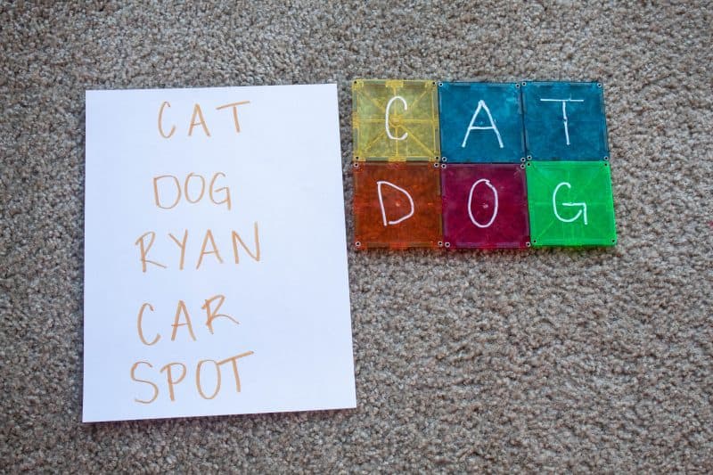 Magnetic tile activity of word creation. A piece of paper with the words "Cat, Dog, Ryan, Car, Spot" written on it. Tiles with the letters C, A, and T and D, O, and G next to it. 