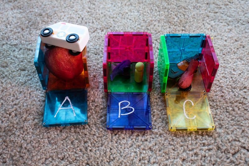 Magnetic tile boxes with the letter A, B, and C written on them and objects that start with each letter inside. An ambulance, apple, bird, boy, car, and cardinal.