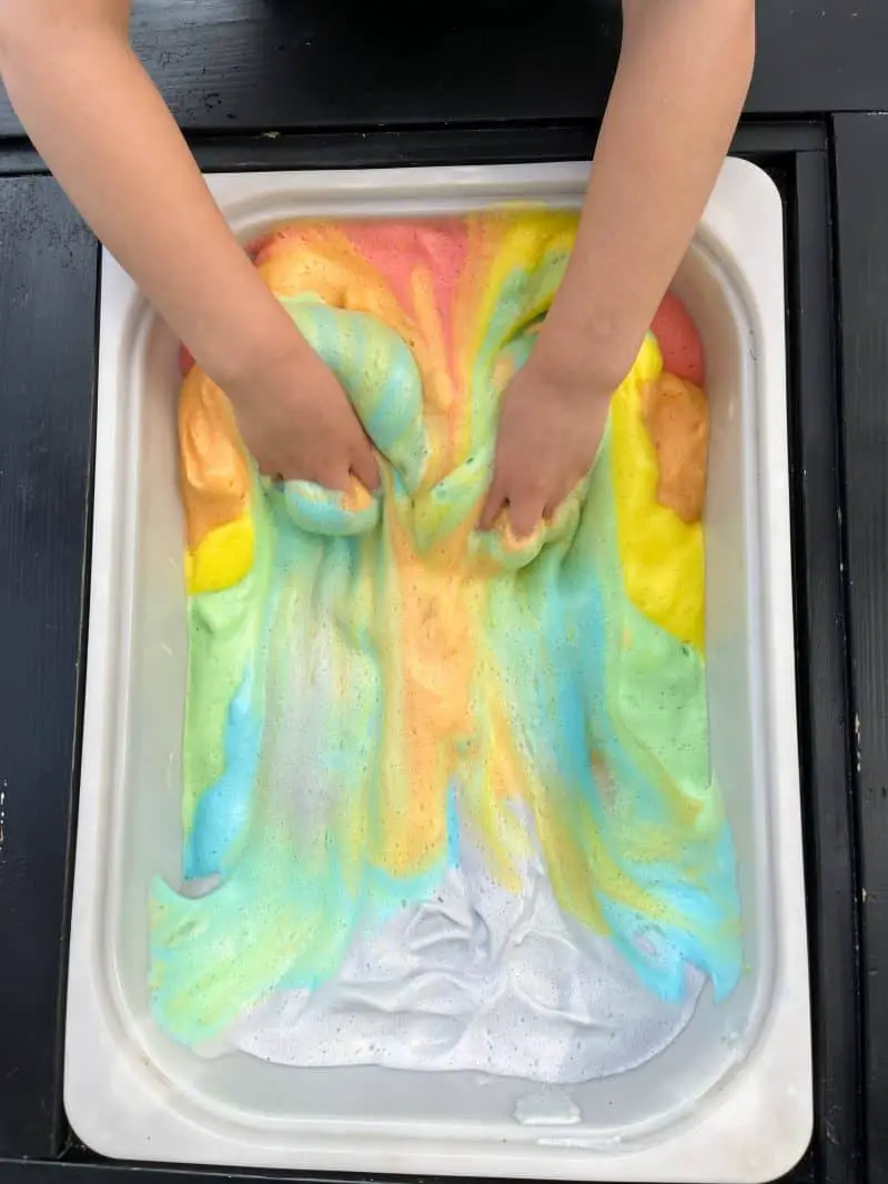 Rainbow aquafaba foam being mixed with together with hands.