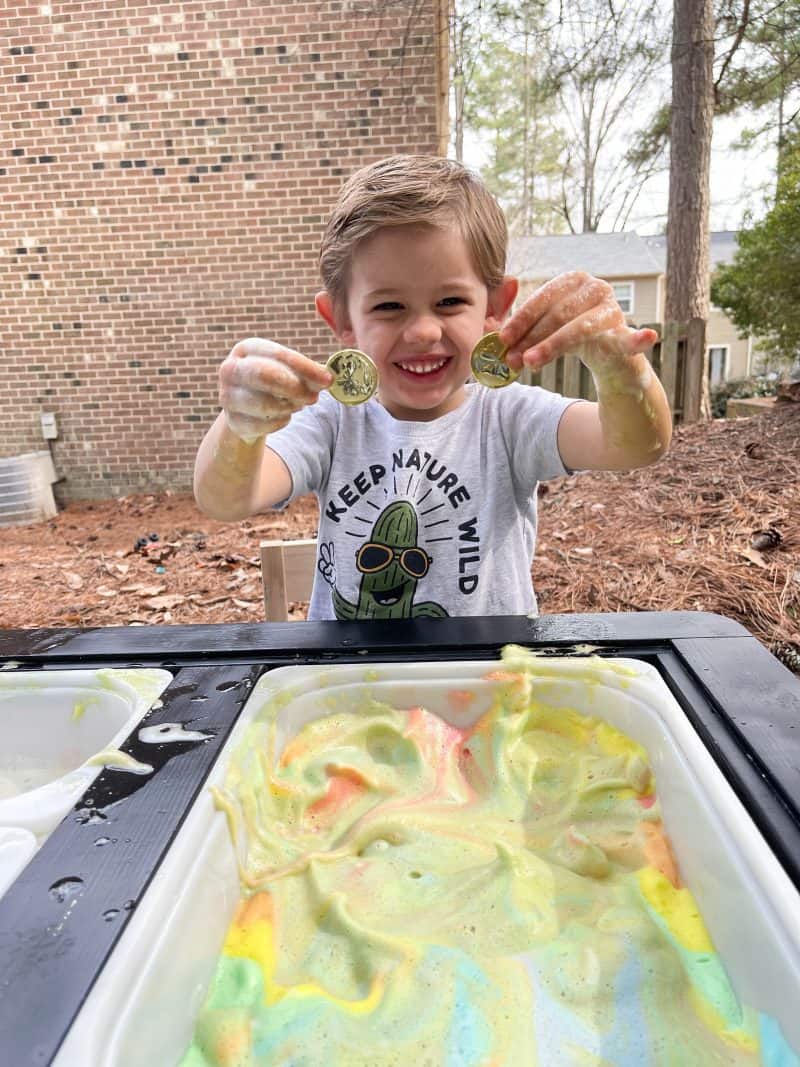 Child playing with rainbow sensory activity finding gold coins in the aquafaba.