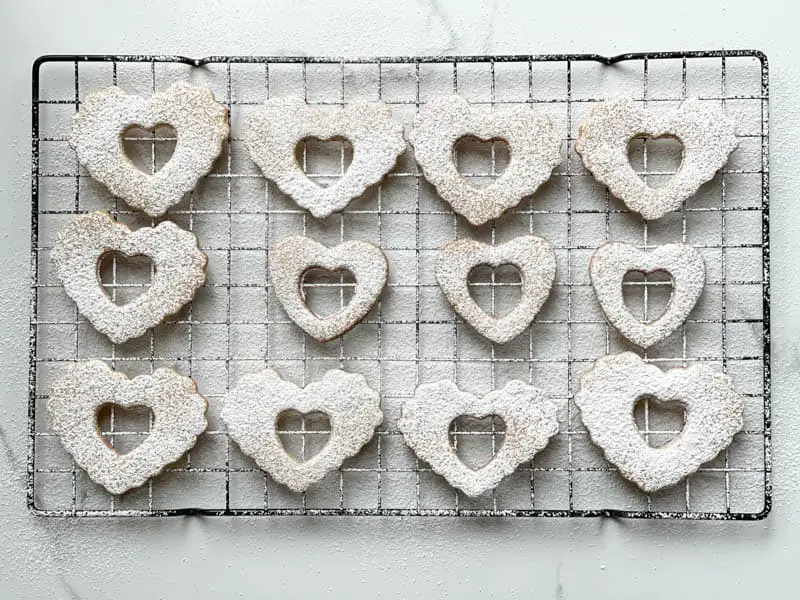 Heart shaped cookies on a cooling rack dusted in powered sugar.