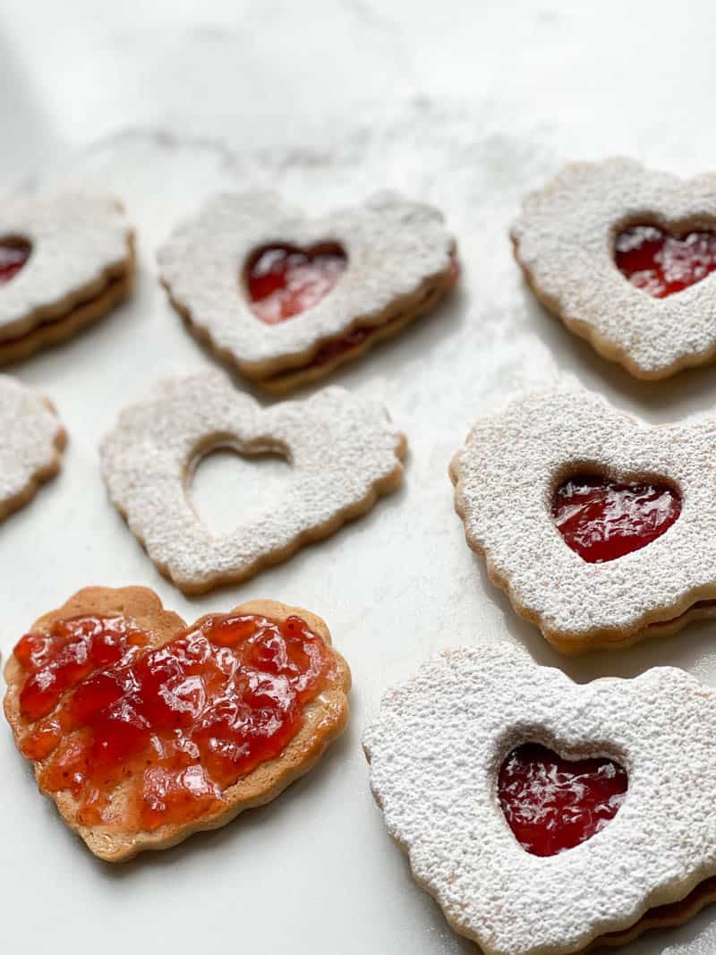 Up close picture of heart shaped cookies dusted in powered sugar and spread with strawberry jam.