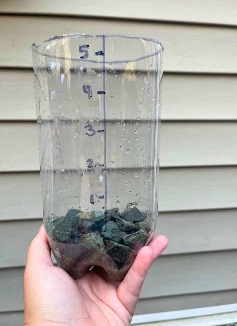 Plastic bottle with measurements on the side and rocks at the bottom