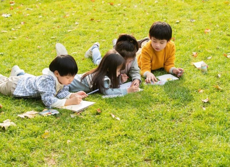 Kids doing outdoor learning activities in the park; coloring notebooks